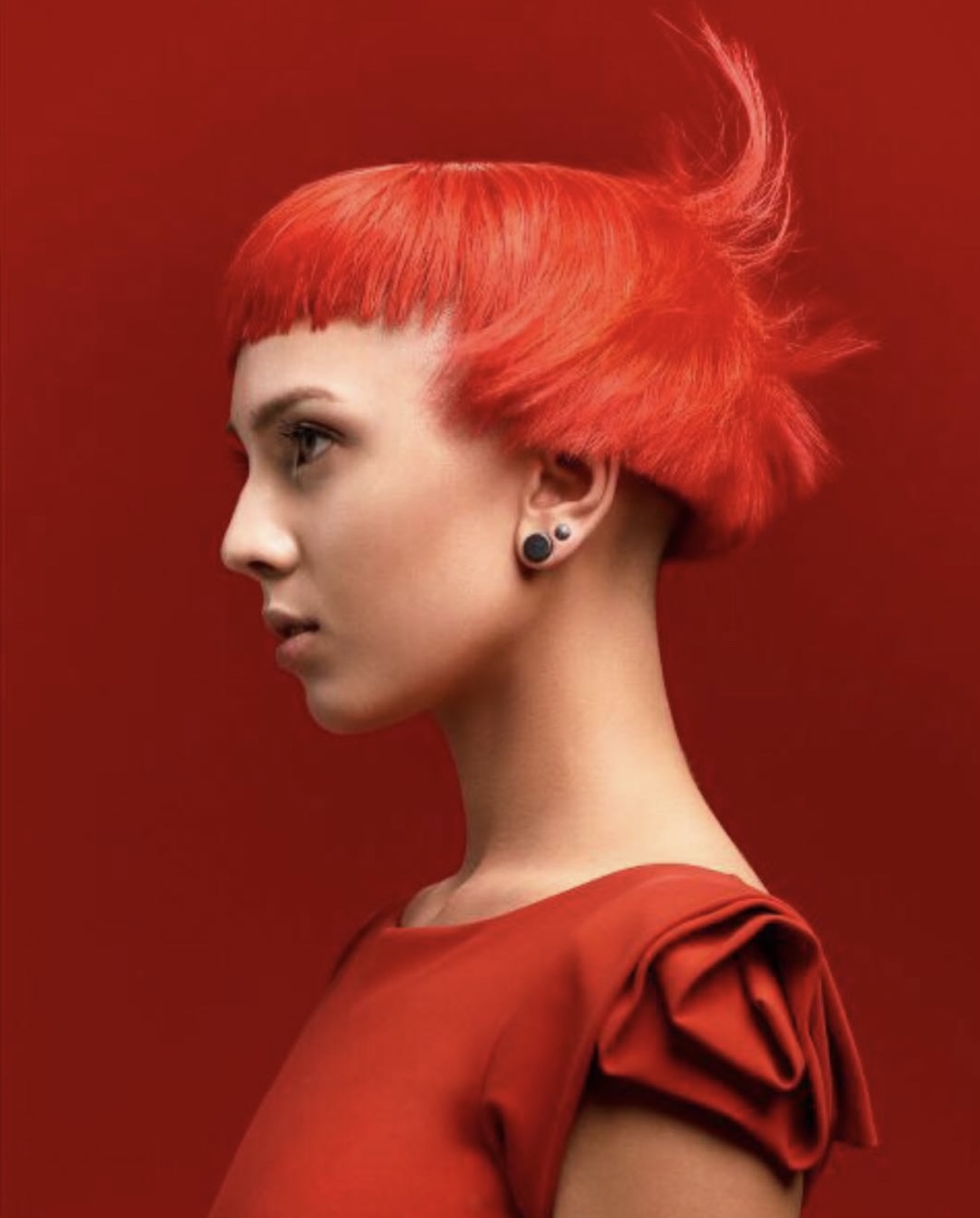 Sideview of a woman with stylish, red haircuit set on a red background